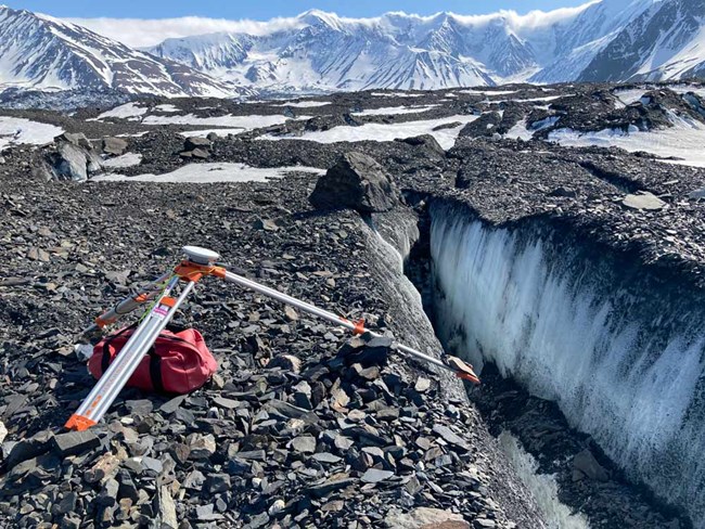 a tripod perched on broken rocks at the edge of a icy crevasse