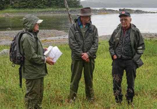 Three people in rain gear stand in green grass.