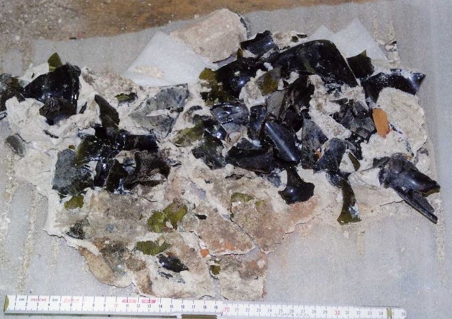 lt= broken bottles of dark brown and green glass held together with white substance