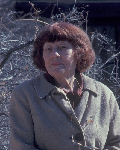 A color portrait of a woman with red hair sitting outside.