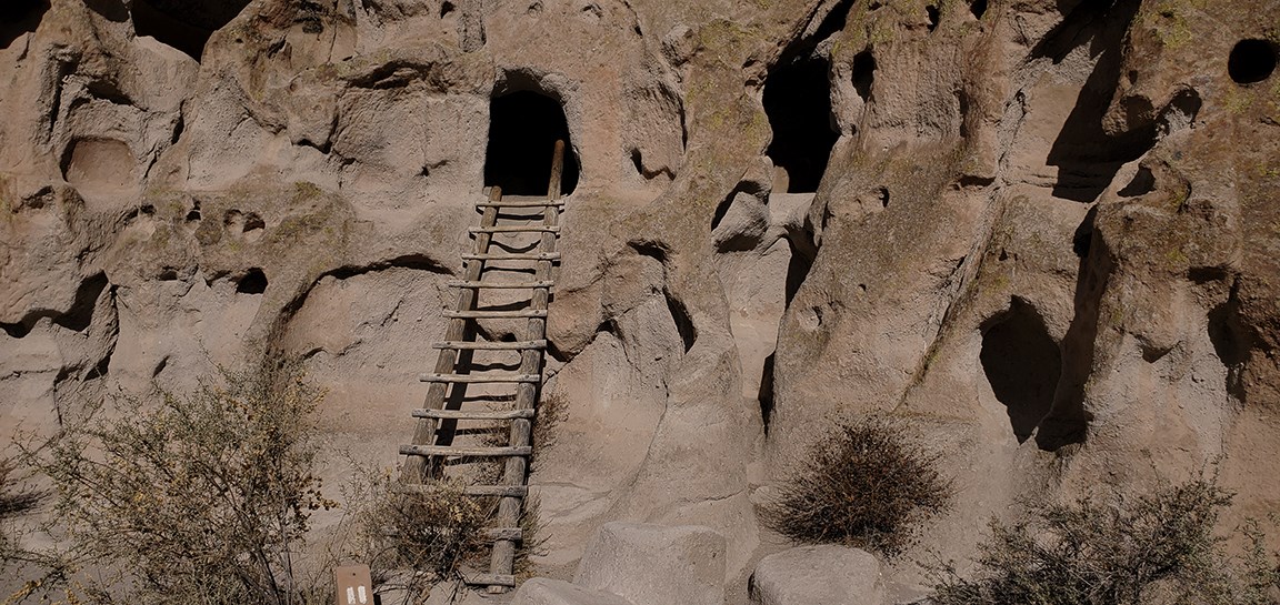 a wooden ladder leans against a beige stone wall with a carved opening