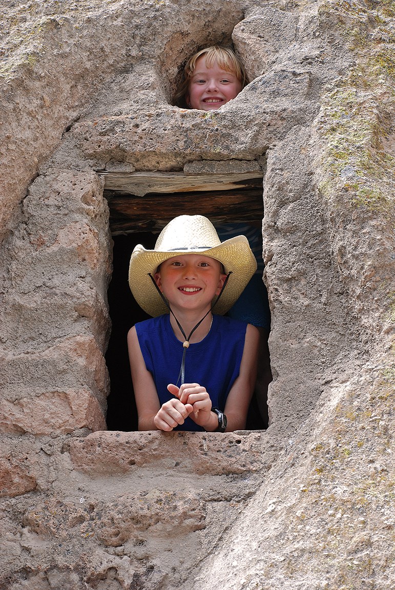 the faces of two children can be seen in openings in the rock wall