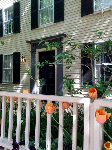 Yellow house with a black door and white picket fence with flowers in front.