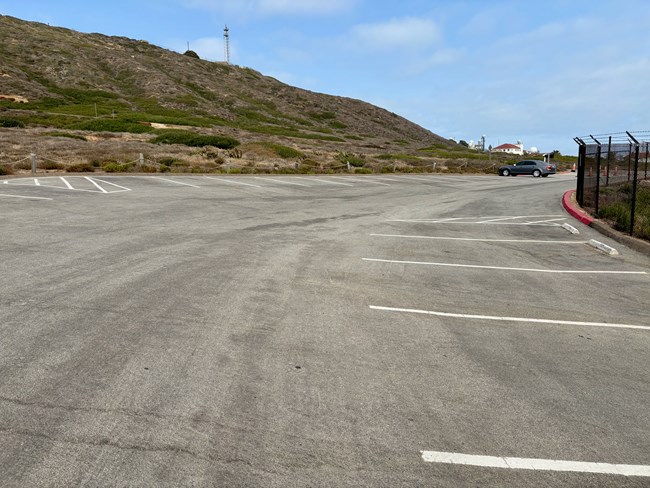 Nearly empty parking lot with one car, hills in the background, and a distant building.