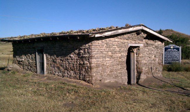 a structure made of sod bricks with a cactus roof stands against a bright blue sky