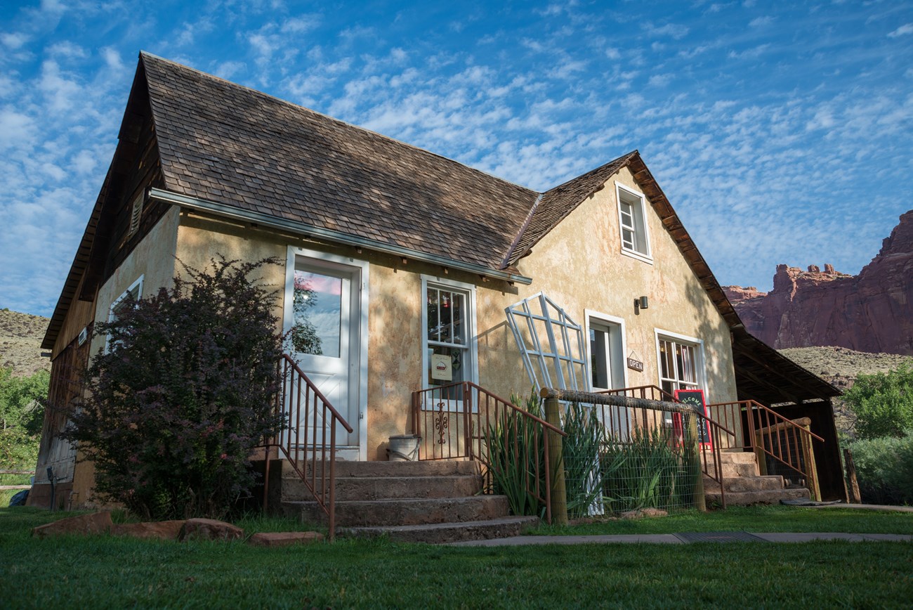 Stucco house with two front doors and small porches, below cliffs with blue sky above.