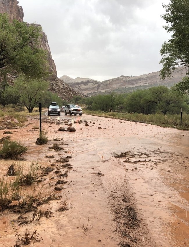 Muddy water and boulders cover a section of paved road.