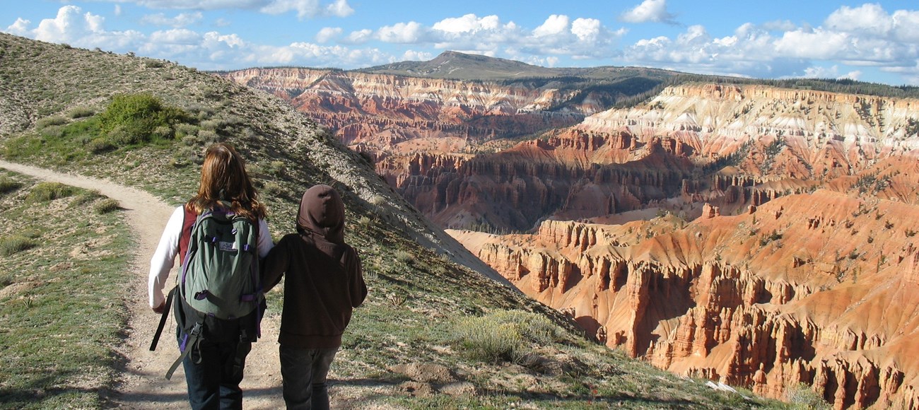 Two people hiking along the rim of the Cedar Breaks Amphitheater.