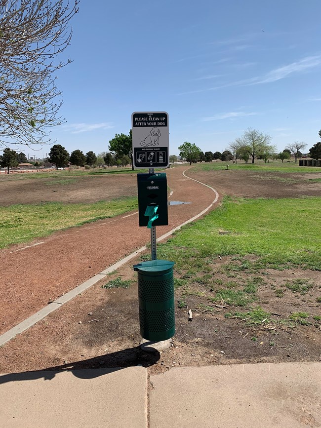 Steel post topped with informational sign, a bag dispenser lower down, and a metal waste bin at the bottom