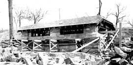 Black and white photo of men constructing a stone building with wood scaffolding surrounding the lower section