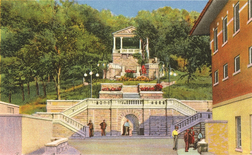 Illustration of a wide stone path with a red brick building on the right. Path leads to an elaborate stone stairway with lamp posts leading up to a hillside with trees and a stone building with columns.