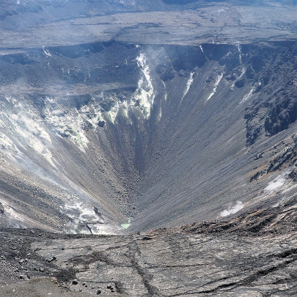 Steaming volcanic crater with small blue pool of water in the bottom