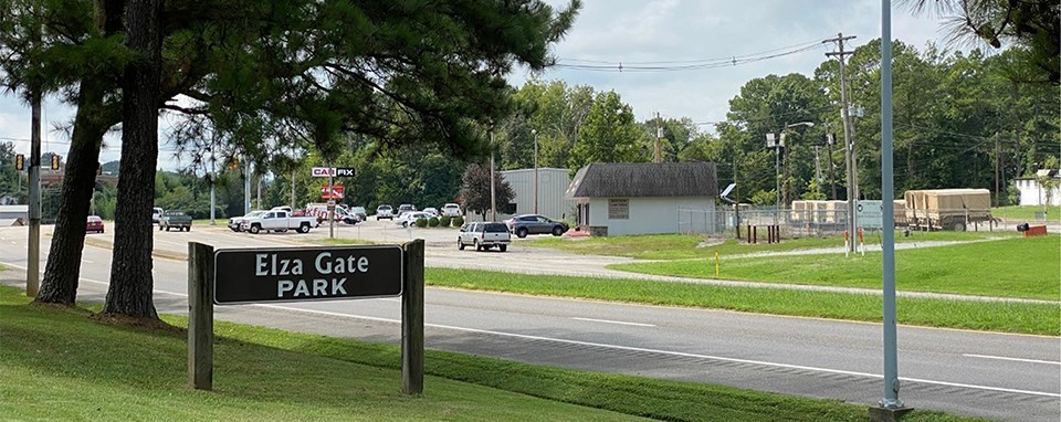 A black and white photo of a car on road going past a gate.