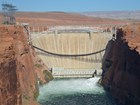 A dam with water at it's base and red cliffs to the left and the right