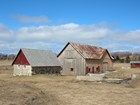 A rural agricultural landscape with wooden farm buildings and open fields.