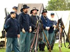 Color photo of several men dressed as soldiers standing with guns.