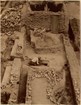 sepia-toned photo of open excavation next to adobe brick building