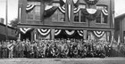 A large group of people gathered in front of three-story brick building on Derby Street.