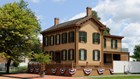 A light orange two story home containing many windows with green shutters.