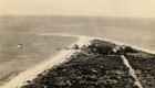 a historic black and white photo of a complex of buildings on the end of an island spit