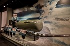 Museum display with a missile against a photo of a mushroom cloud.