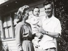 Black and white photo of young couple with baby in front of house