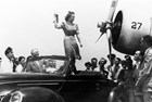 Black and white photo of a woman christening a propeller plane