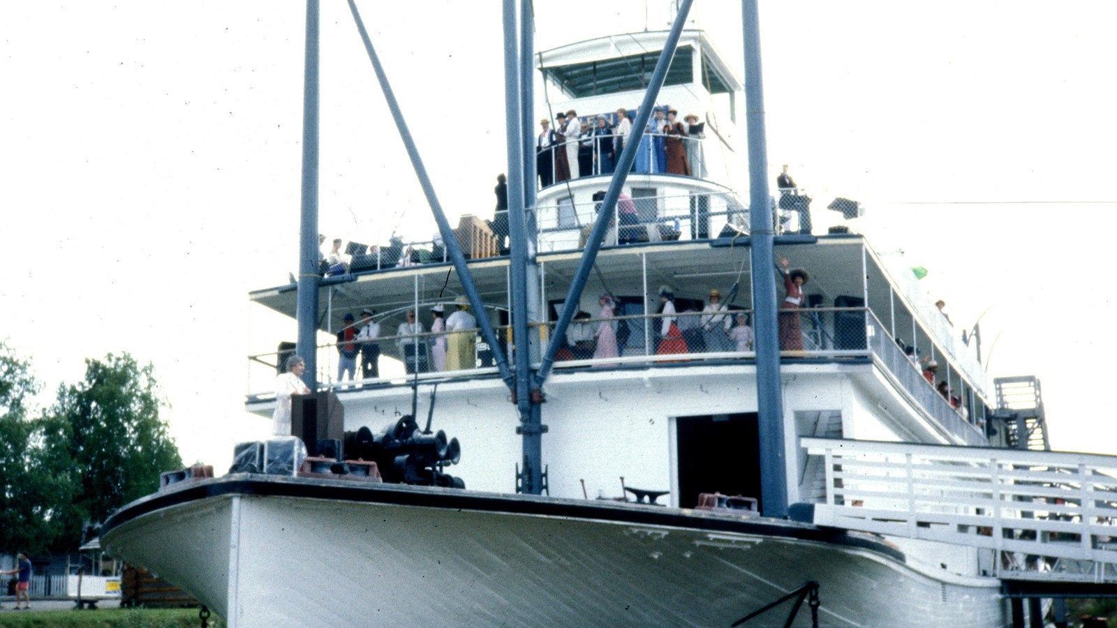 A white sternwheel paddle ship with actors dressed in early 20th century period costumes aboard.