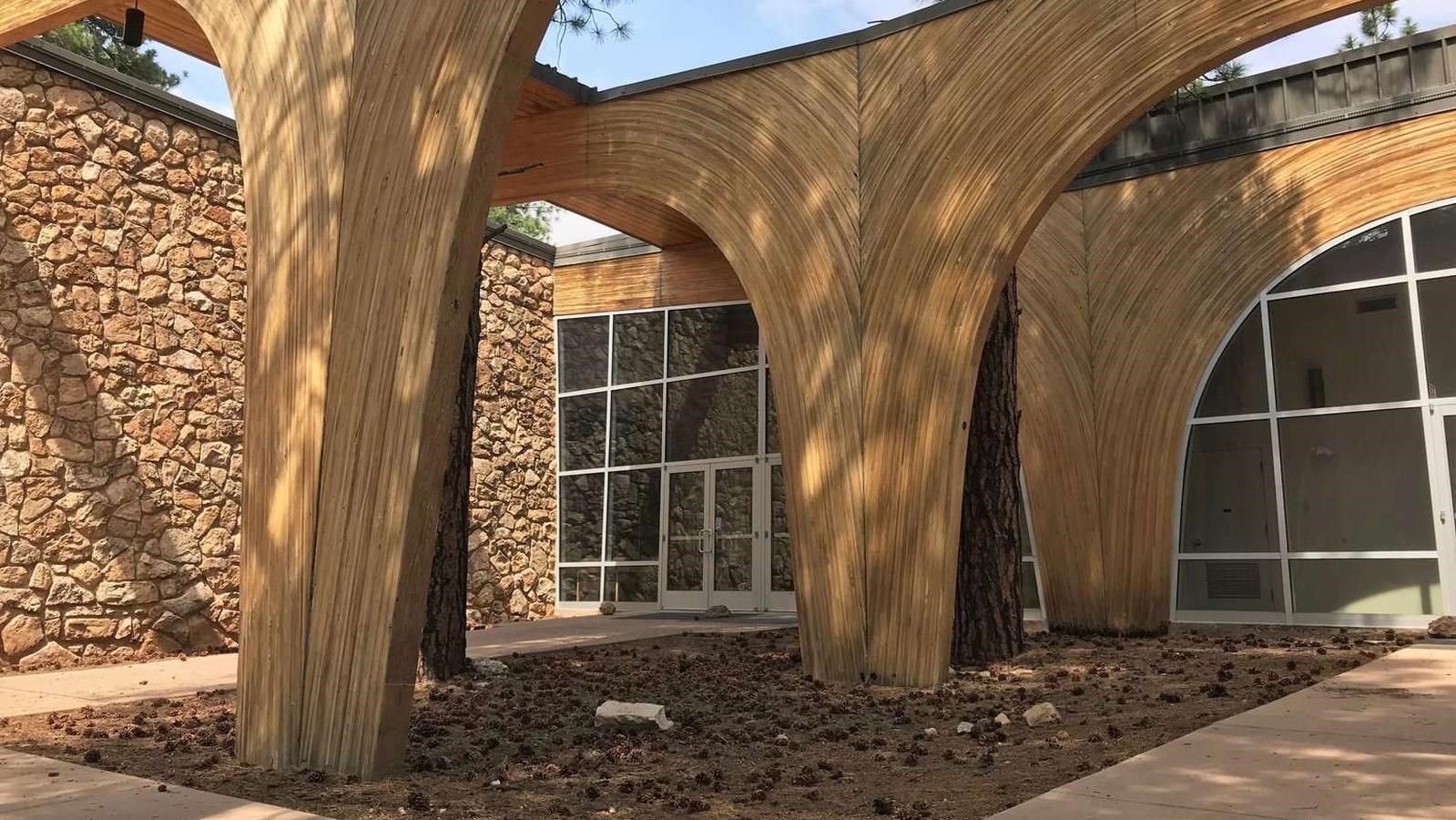 A modern 2 story building with stone walls and large wooden entryway arches and large glass windows