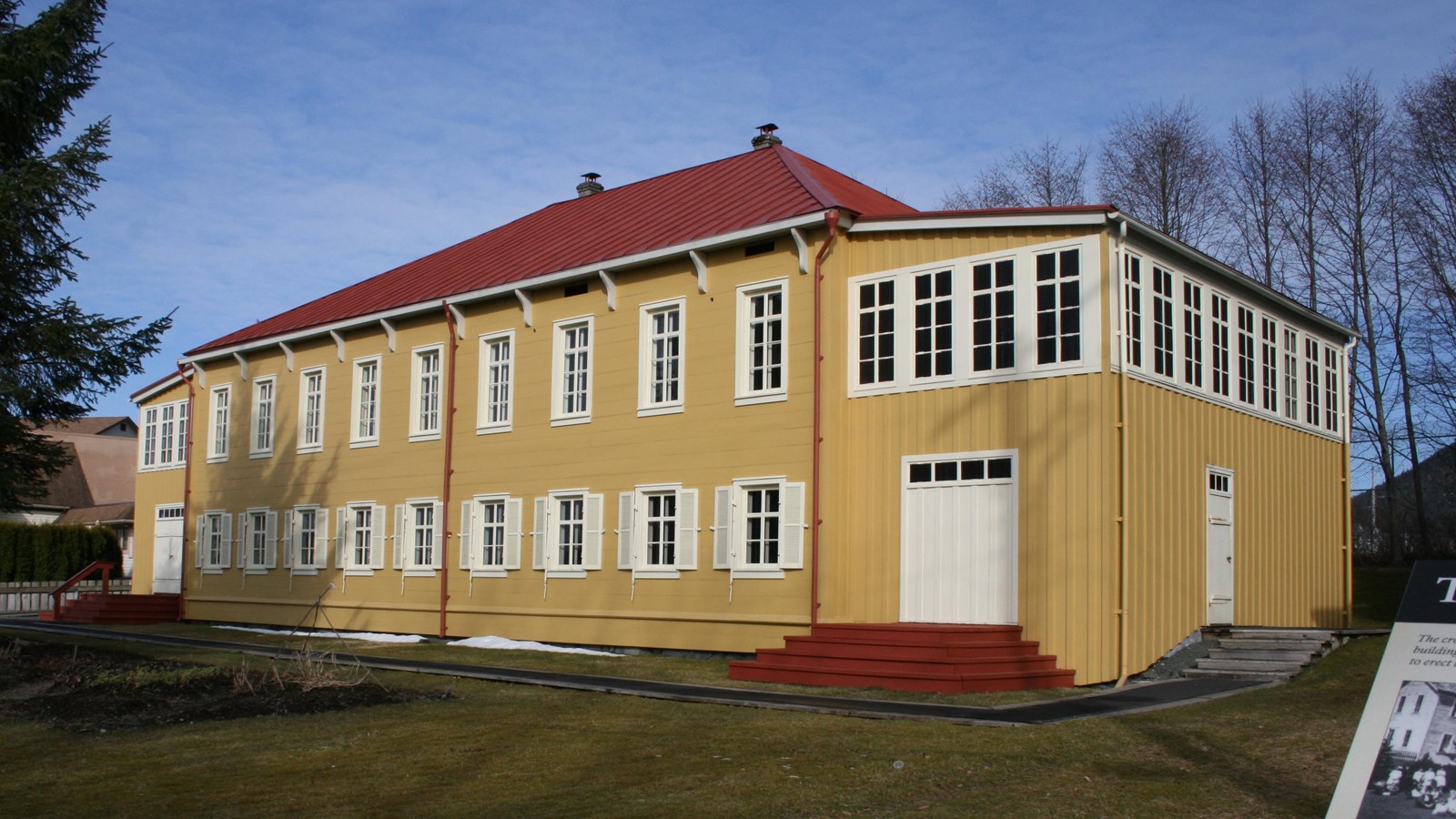 A two story yellow building with a red roof and white trimmed windows and doors.