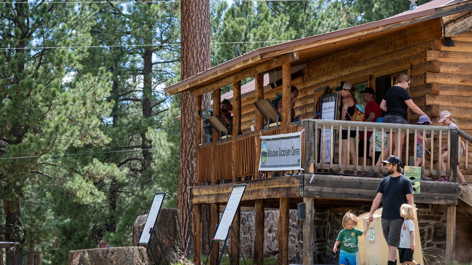 People on the covered front porch of a log building.