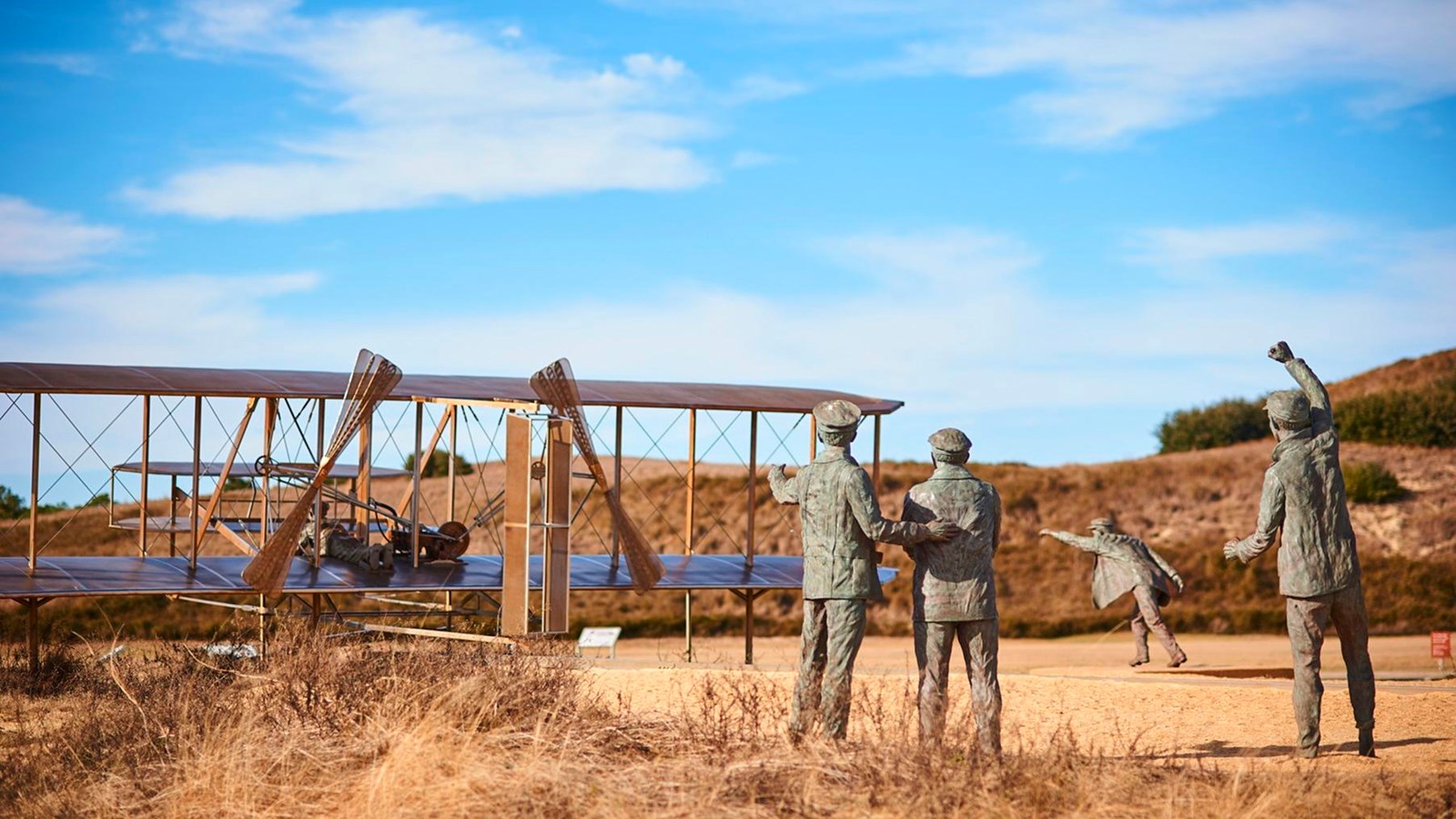 Bronze sculpture of 4 men next to a Wright Flyer cheering it on