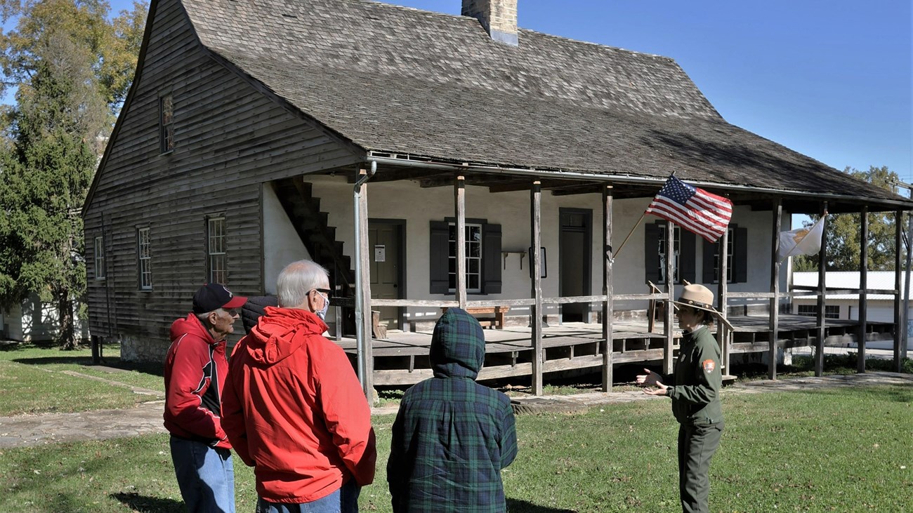 Park Ranger giving a tour in front of a old home with a front porch. 