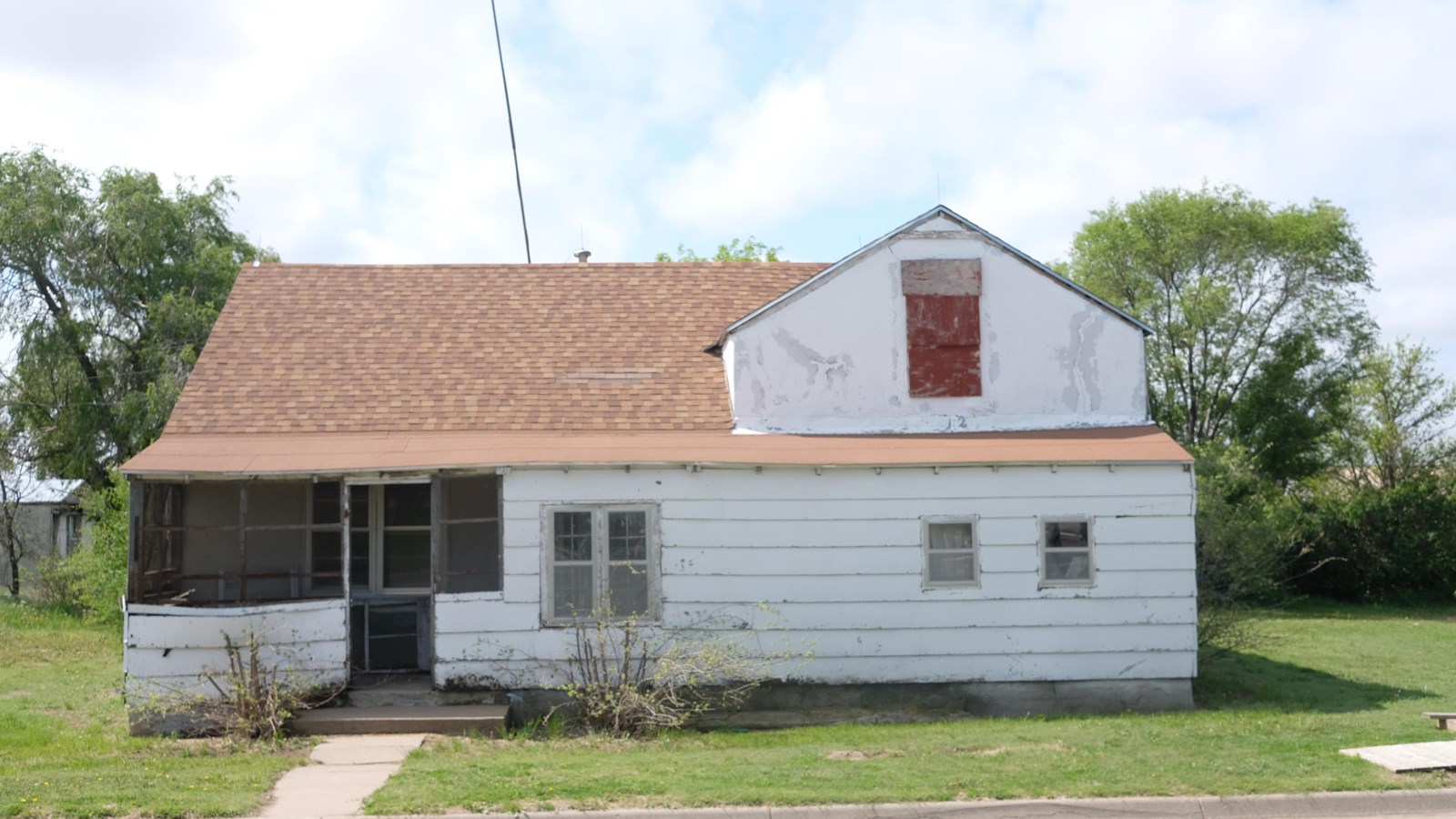 White two-story building with a screened porch on green lawn with trees in the background