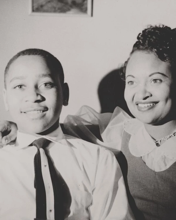 Two African Americans sit and smile toward the camera. A woman, at right, has a arm around a boy.,
