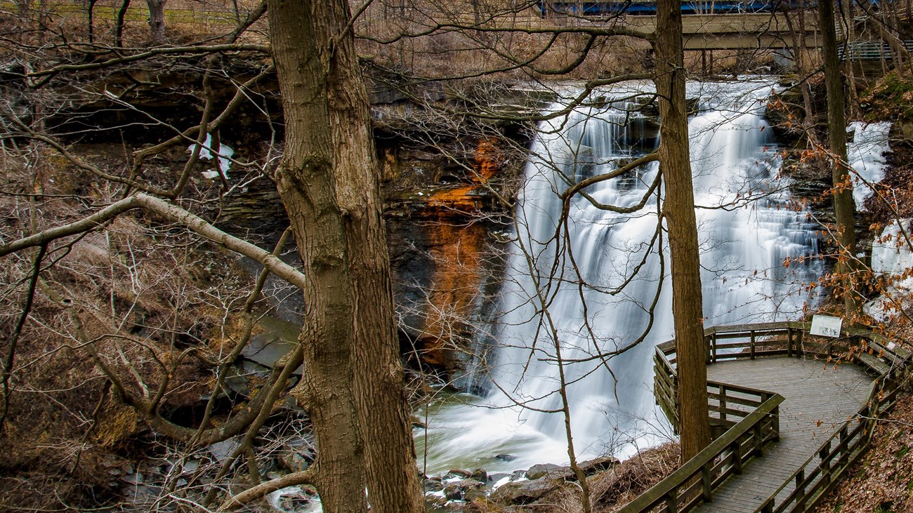 View down through bare trees at a deck overlooking a waterfall cascading into a gorge.