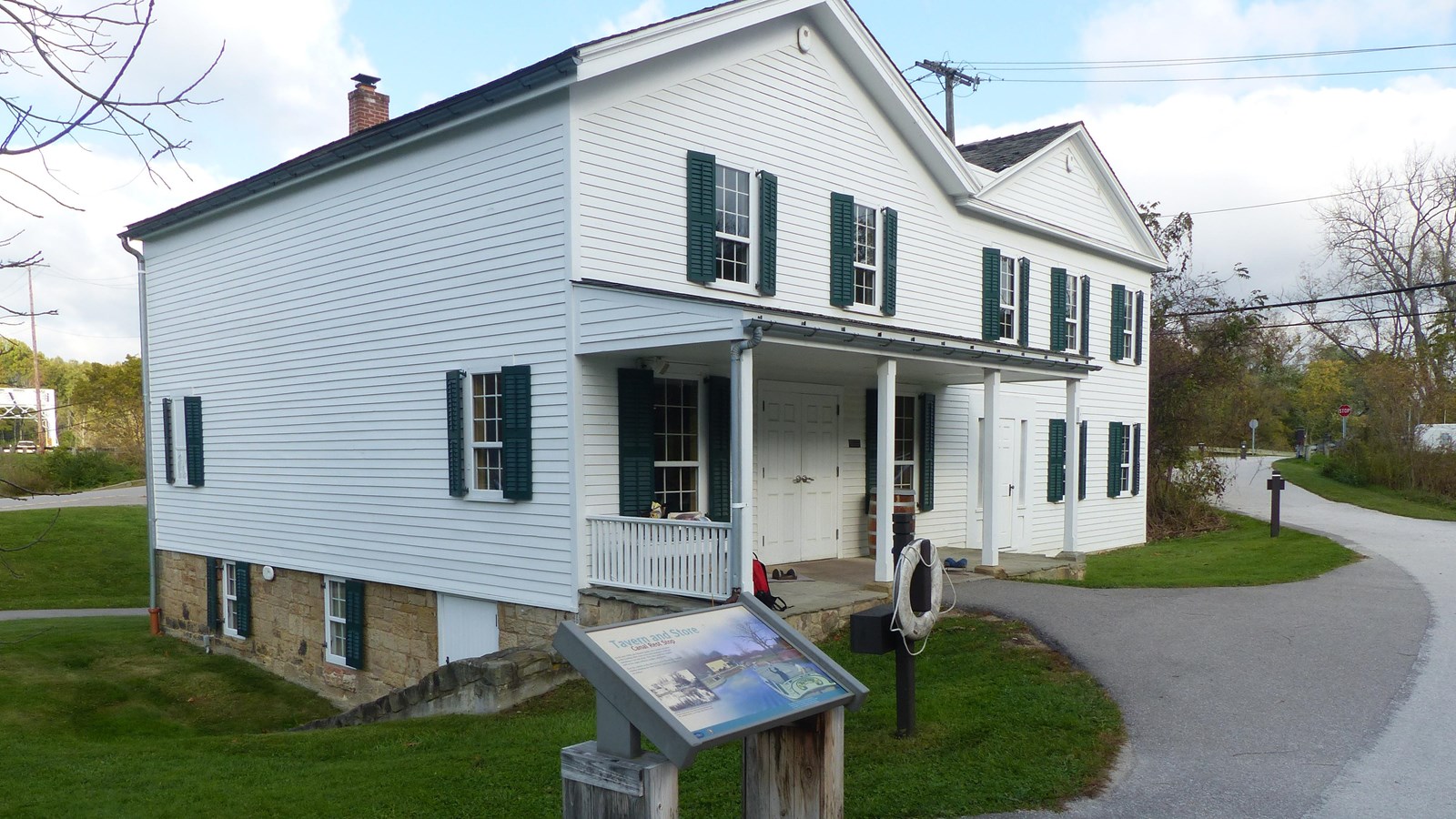  A graphic panel and life ring stand ouside a white historic  building with a porch and an M-shaped 