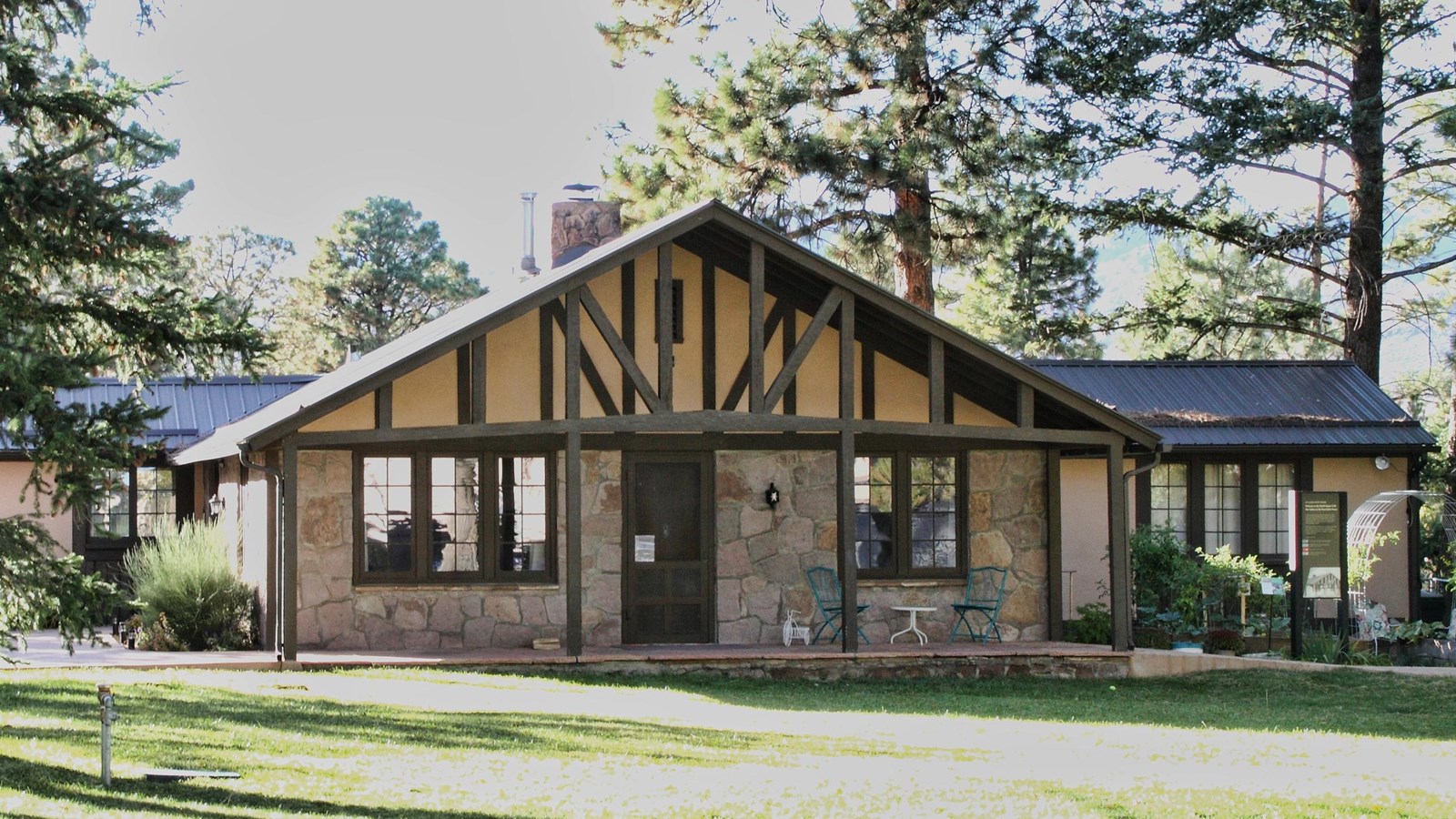 A stucco and timber house sits on a grassy lawn with trees around it.