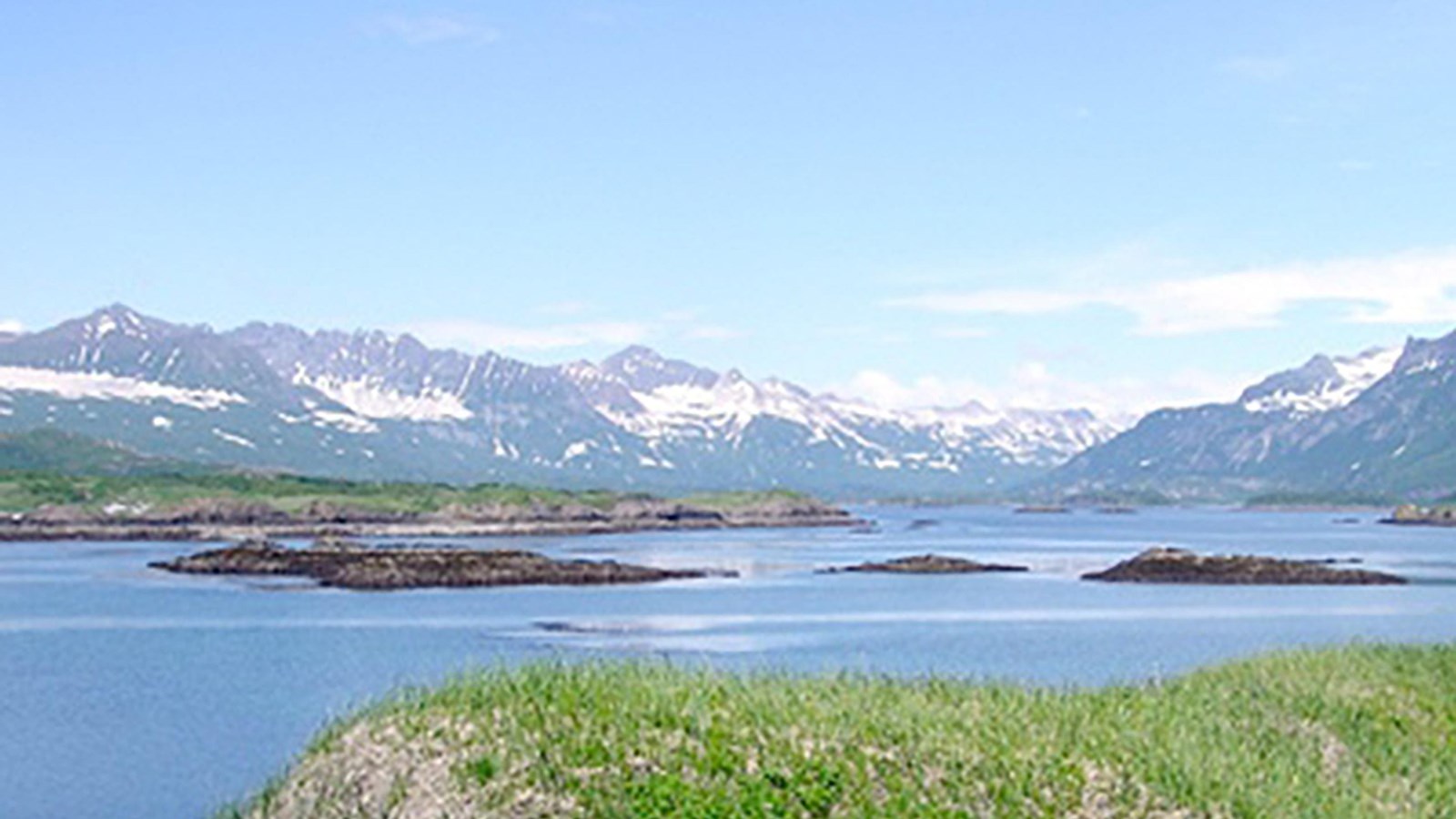 Tiny islands in a bay with snow covered mountains on the horizon.