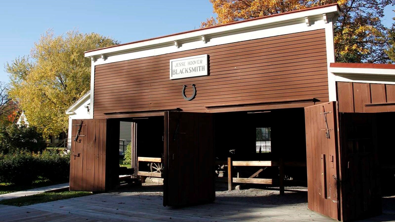 A low brown barn-like building with three large doorways has a large horseshoe on its facade. 