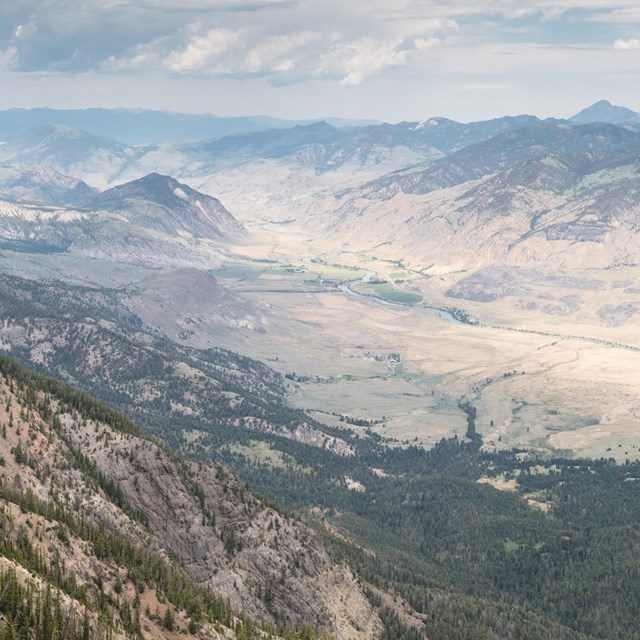 A man stand on a cliff with mountains in the distance