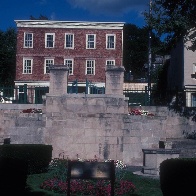 2 large stone pillars center. A large 3 story brick house dominates the far view of the photo.  