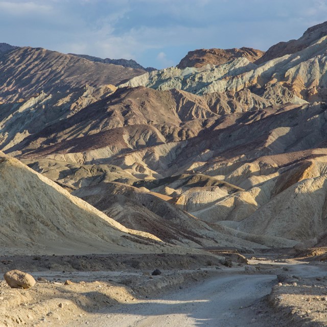 A dirt road leads into multi-hued eroded desert hills. 