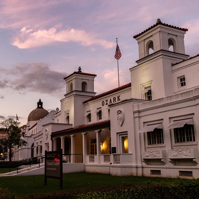 A white, hacienda style bathhouse takes on pink and purple hues as the sun sets.