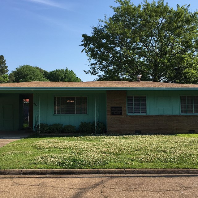 A small ranch-style brick and teal-sided home sits quietly on manicured lawn.