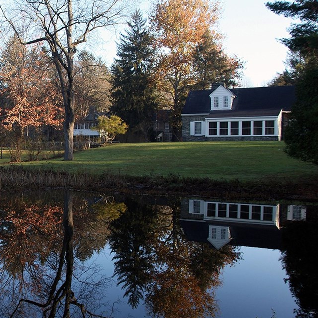 A shiny pond with a white cottage in the background. Autumn leaves reflect in the water\'s surface. 