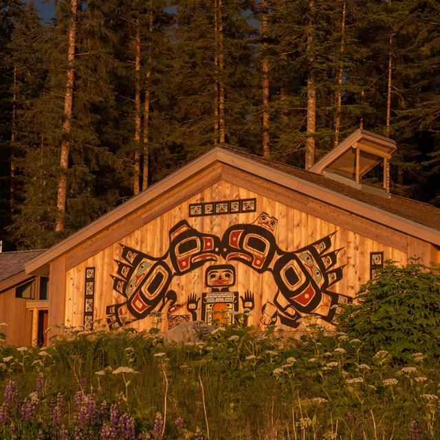 Building in forest with brightly colored stylized birds painted on the outside wall.