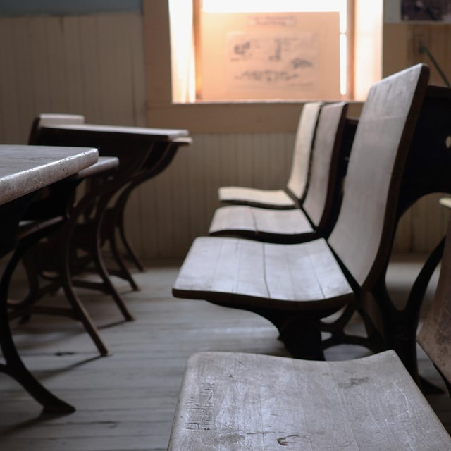 Looking down a row of old wooden empty school seats with desks on the left.