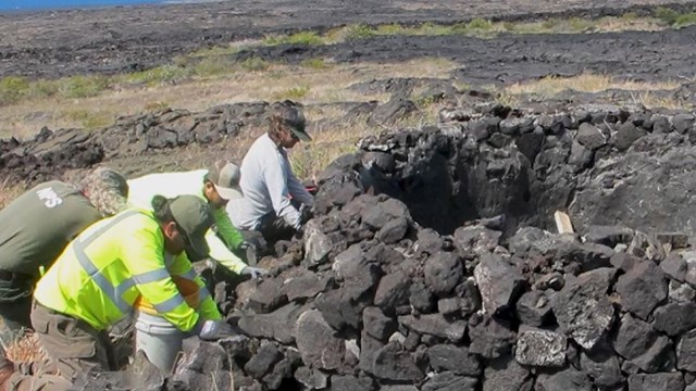 Four limestone workers dig on their knees in front of a limestone deposit. Photo from HAVO video.