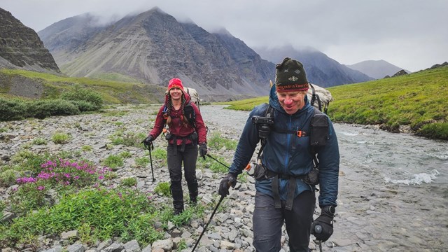 Two backpackers walk along a creek